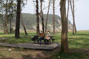 Aged caucasian couple 70-80 sitting in a recreational area with eucaliptus and pine trees near Rodiles beach. photo