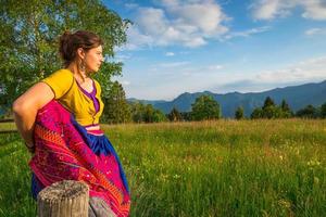 Casual girl relaxes doing stretching and yoga alone in the mountains over a fence in a beautiful spring meadow. photo