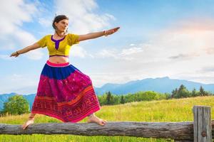 Casual girl relaxes doing stretching and yoga alone in the mountains over a fence in a beautiful spring meadow. photo