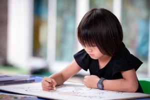 Asian student girl doing art on big paper. Child holding oil pastel color and fun coloring. Kid make craft at home. Hobby with activity at homeschool. photo