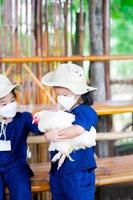 Portrait of little girl holding big hen. Preschool girl wearing surgical 4D white face mask. photo