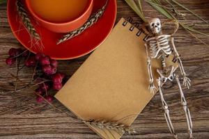 Halloween card with skeleton and notepad. Autumn background with rowan and a cup of pumpkin juice. photo