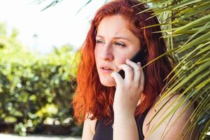 Close up of serious girl with redhead talking on mobile phone while standing outdoors photo