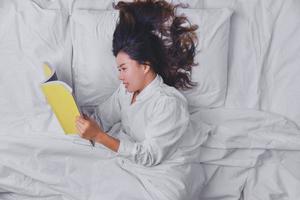 mujer joven durmiendo en la cama. vista superior de la mujer joven acostada durmiendo en la cama. durmiendo relajarse, joven sonriente bonita dama yace en la cama. dormir, leer un libro en la cama. educación, lectura. foto