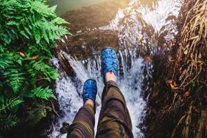 Asian woman travel nature. Travel relax. Top view of the girl's legs wearing blue shoes. She is lifting her legs floating on the waterfall. nature, background, summer, holiday, tourist. photo