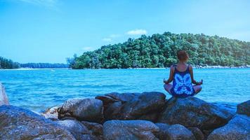 las mujeres asiáticas se relajan en las vacaciones. viajar relajarse. jugar si yoga. sobre las rocas junto al mar. en el verano. tailandia foto