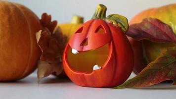 A lamp in the form of a pumpkin for Halloween, against the background of autumn leaves and pumpkins. video