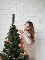 young attractive woman decorating the Christmas tree with fairy lights photo