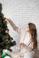 young attractive woman decorating the Christmas tree with fairy lights photo