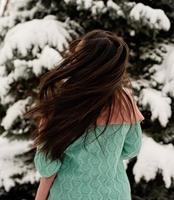 Vista posterior de la mujer morena en ropa de invierno rosa de pie al aire libre en un día de nieve por el árbol de Navidad foto