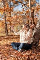 Mujer joven arrojando hojas amarillas en el aire sentado en el bosque de otoño foto