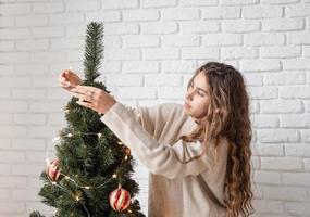 young attractive woman decorating the Christmas tree with fairy lights photo