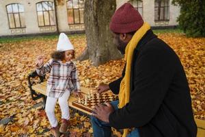 Abuelo y nieta negros jugando al ajedrez en el parque de otoño