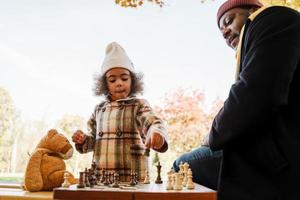 Abuelo y nieta negros jugando al ajedrez en el parque de otoño foto