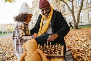 Abuelo y nieta negros jugando al ajedrez en el parque de otoño