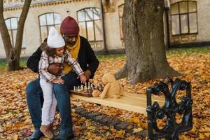 Black grandfather and granddaughter playing a game of chess in an autumn park photo