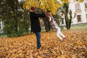 Black grandfather and granddaughter making fun while playing together in autumn park photo