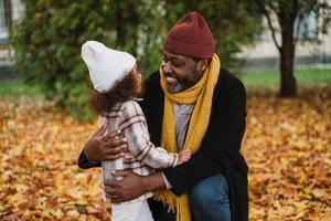 Abuelo y nieta negros abrazándose y sonriendo en el parque de otoño foto