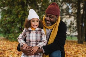 Black grandfather and granddaughter hugging and smiling in autumn park