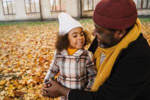 Black grandfather and granddaughter making fun while playing together in autumn park photo