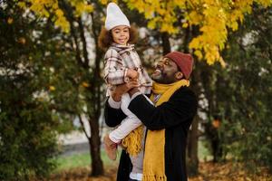 Chica negra divirtiéndose y sentada en el cuello de su abuelo en el parque de otoño