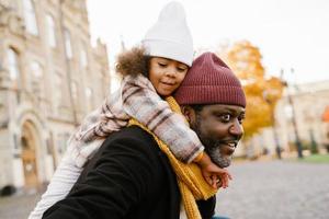 Black grandfather and granddaughter smiling while walking together in autumn park photo