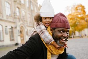 Black grandfather and granddaughter smiling while walking together in autumn park photo