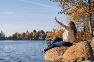 Mujer romántica pensativa sentada sobre las rocas en la orilla del río al atardecer en el día de otoño foto