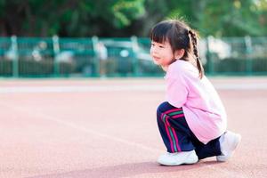 Kindergarteners squat in a sports ground, pretending to run. Happy child sweet smiles. Active children 3-4 years old wear pink shirts and sports shoes. photo