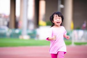 Active child running at the stadium.  Happy kid exercise and have fun laughing. Sweet smile cute girl. She wearing pink shirt. Baby aged 3-4 year old. photo
