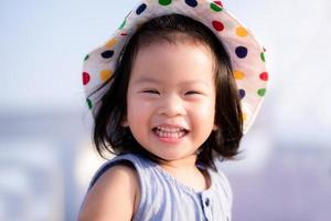 Asian baby child girl beaming smiling. Close up happy face. Little girl wearing white hat. Half body photo. She has tooth decay. Baby age 2 years and 9 month old. photo