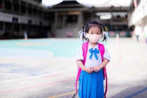 Child back to school concept. Girl wearing cloth face mask. Kid shoulder pink bag. Children wearing student uniform. Baby aged 3-4 year old. photo