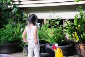 La espalda de la niña asiática ayuda a la familia con las tareas del hogar. La niña se prepara para regar las plantas con una regadera amarillo-roja colocada a su lado. concepto de enseñar a los niños a asumir responsabilidades.