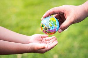 The hands of adults are passing the world to the hands of children, to continue to care and heal our planet. Blurred green grass background. Earth Day Concept . photo