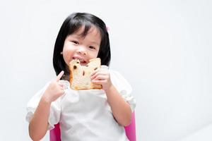 Adorable child holding Raisin Bread Slices. Kid pointing index finger at food. Happy girl sweet smile. Children enjoy eating. On white background. photo