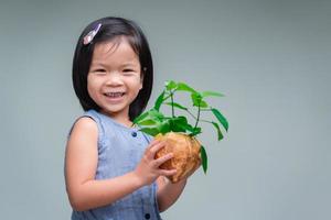 Child holds plant that has been planted in pot. Isolated background. Sweet smiling kid. Concept of saving the world. Nature Conservation Day. Environment day. photo