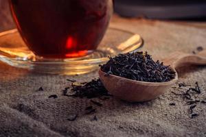 dry tea leaves in a wooden spoon and brewed in a glass cup of tea on a background of burlap photo