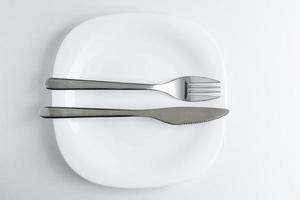 The fork and knife lie on a white plate on a light background. photo