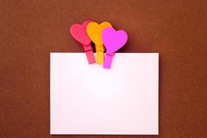 Small colored hearts hold a paper note on a brown background photo