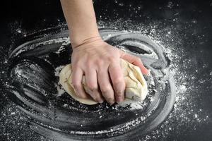 The man kneads dough on a black table sprinkled with flour. photo