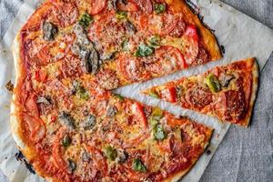 homemade delicious pizza with salami, tomatoes and mushrooms, cut into pieces on a dark background of sacking photo