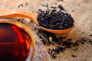 Secar las hojas de té en una cuchara de madera y una taza de té sobre arpillera a contraluz. foto