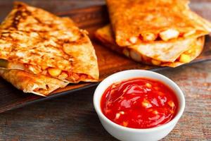 two pieces of quesadilla on a plate and sauce of salsa on a wooden background. National Mexican cuisine photo