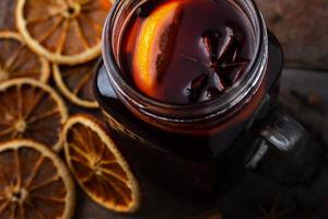 Copa de vidrio con vino caliente con naranjas secas y especias sobre una mesa de madera foto