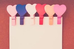 Small colored hearts hold a paper note on a brown background photo