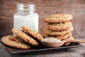 Homemade oat biscuits with sesame seeds and seeds and a mug of milk on a wooden background photo