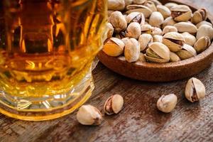 a glass of light beer and a handful of pistachios on a wooden table