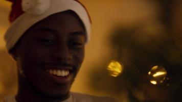 Close up of smiling man with Christmas hat decorating Christmas tree with bauble video