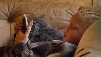 Boy lying on his back on sofa looking at smartphone video