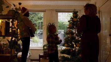 Mann spielt Gitarre mit Weihnachtsmütze und Mädchen und Frau, die den Weihnachtsbaum schmücken